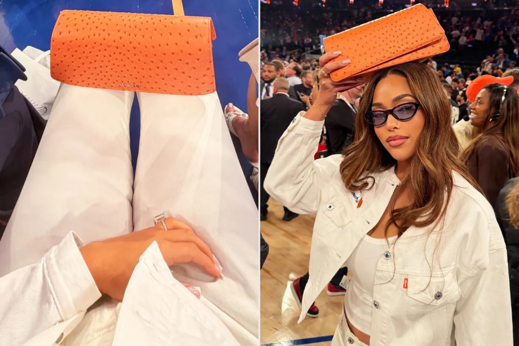 A person wearing a white jacket and holding an orange clutch purse in a crowded event venue.
