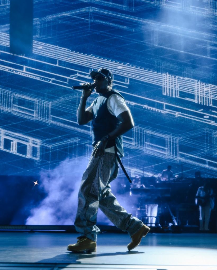 A person wearing a white shirt and dark pants performing on a stage with a blue-tinted background and lighting.