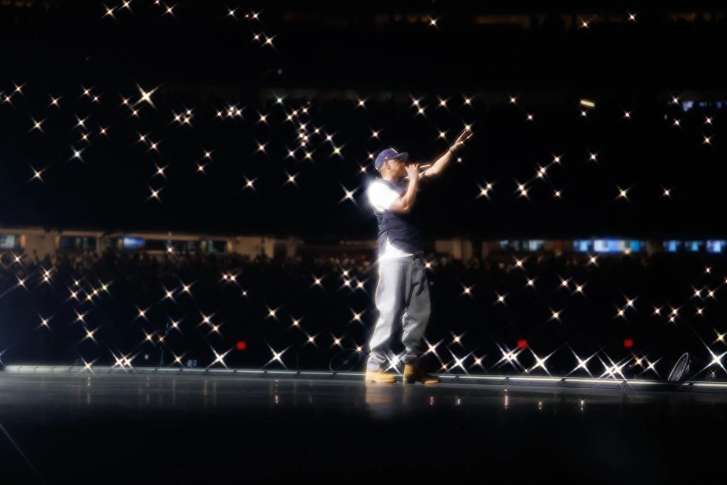 A performer on stage at night, arms raised, surrounded by a starry night sky of twinkling lights.