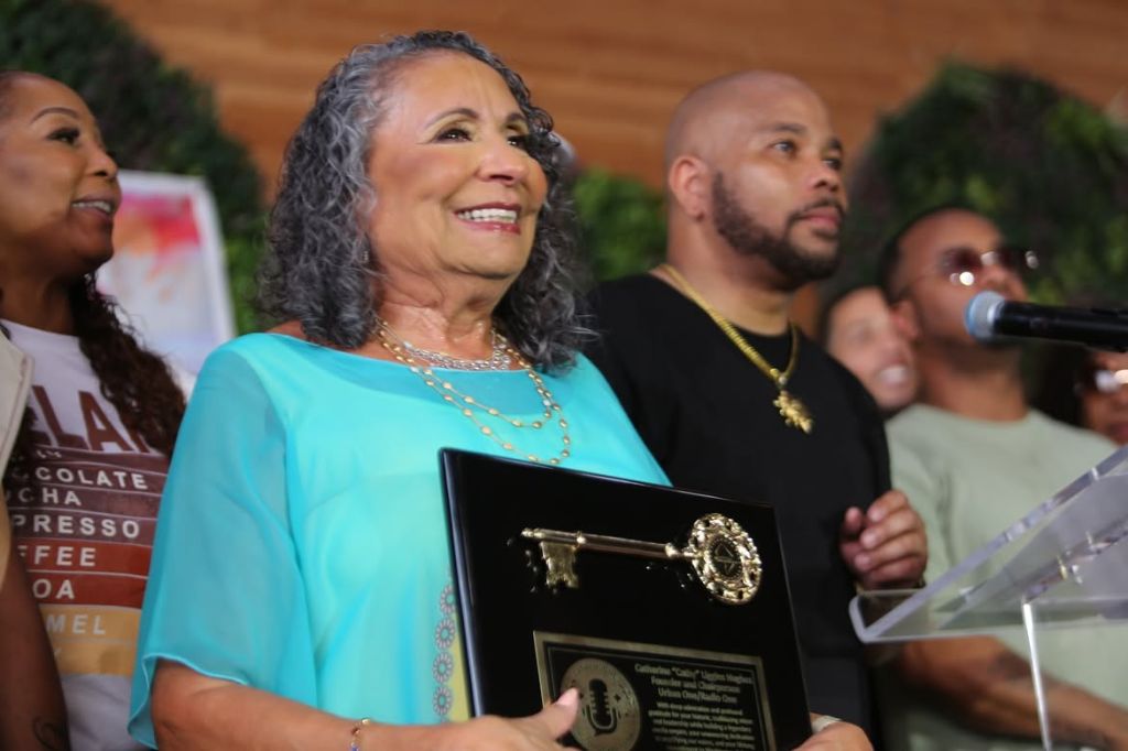 A smiling older woman holding an award plaque, surrounded by a group of people.