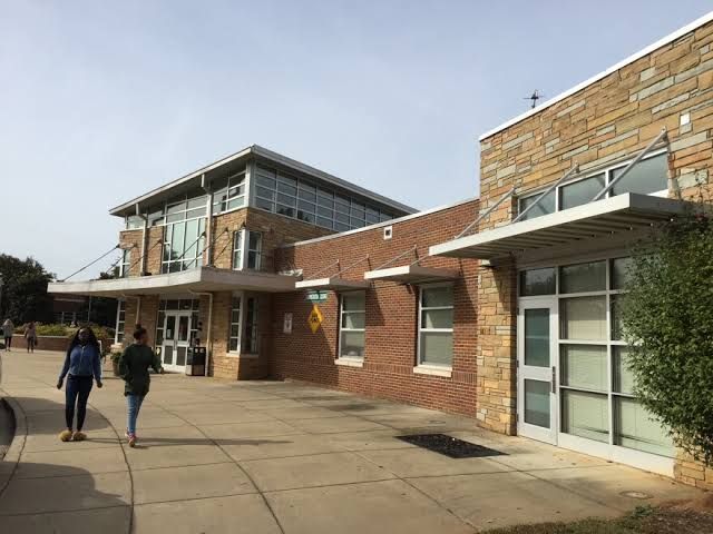 A brick building with glass windows and a covered walkway, with people walking on the sidewalk in front of it.