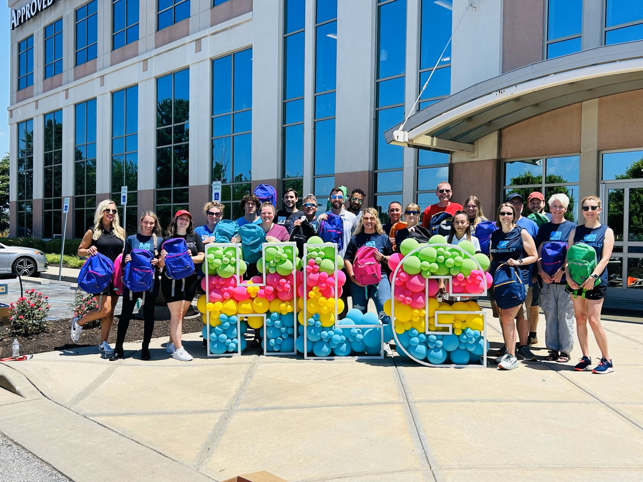 A group of people holding colorful balloon displays in front of a commercial building with the word "Approved" visible.