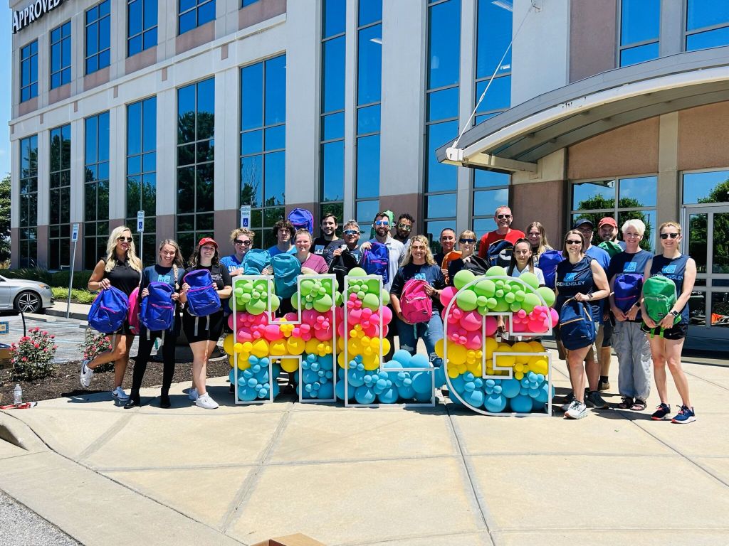 A group of people holding colorful balloon displays in front of a commercial building with the word "Approved" visible.