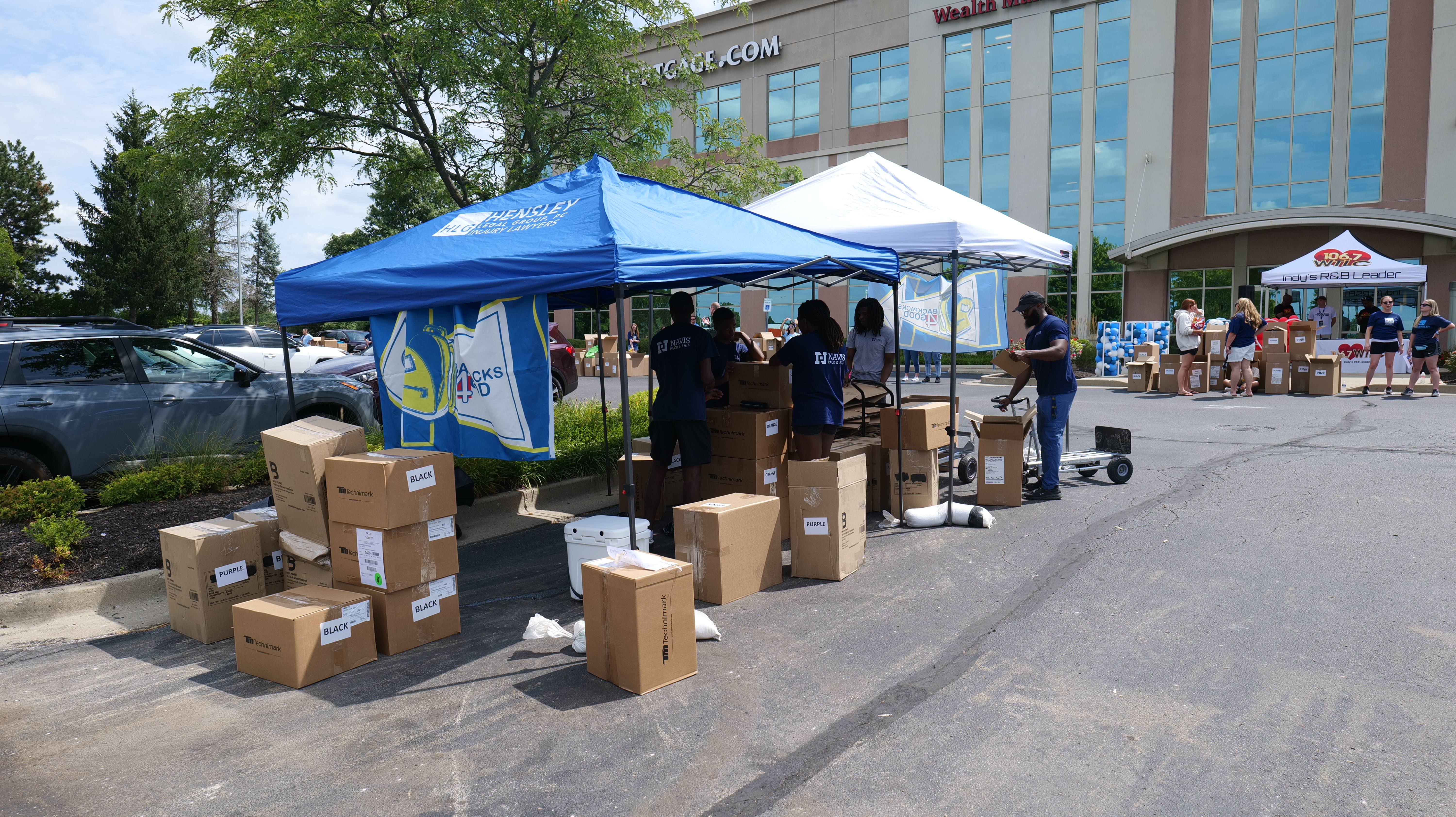 Outdoor tent with "Acme" logo, boxes and people at a community event or donation drive in a parking lot.