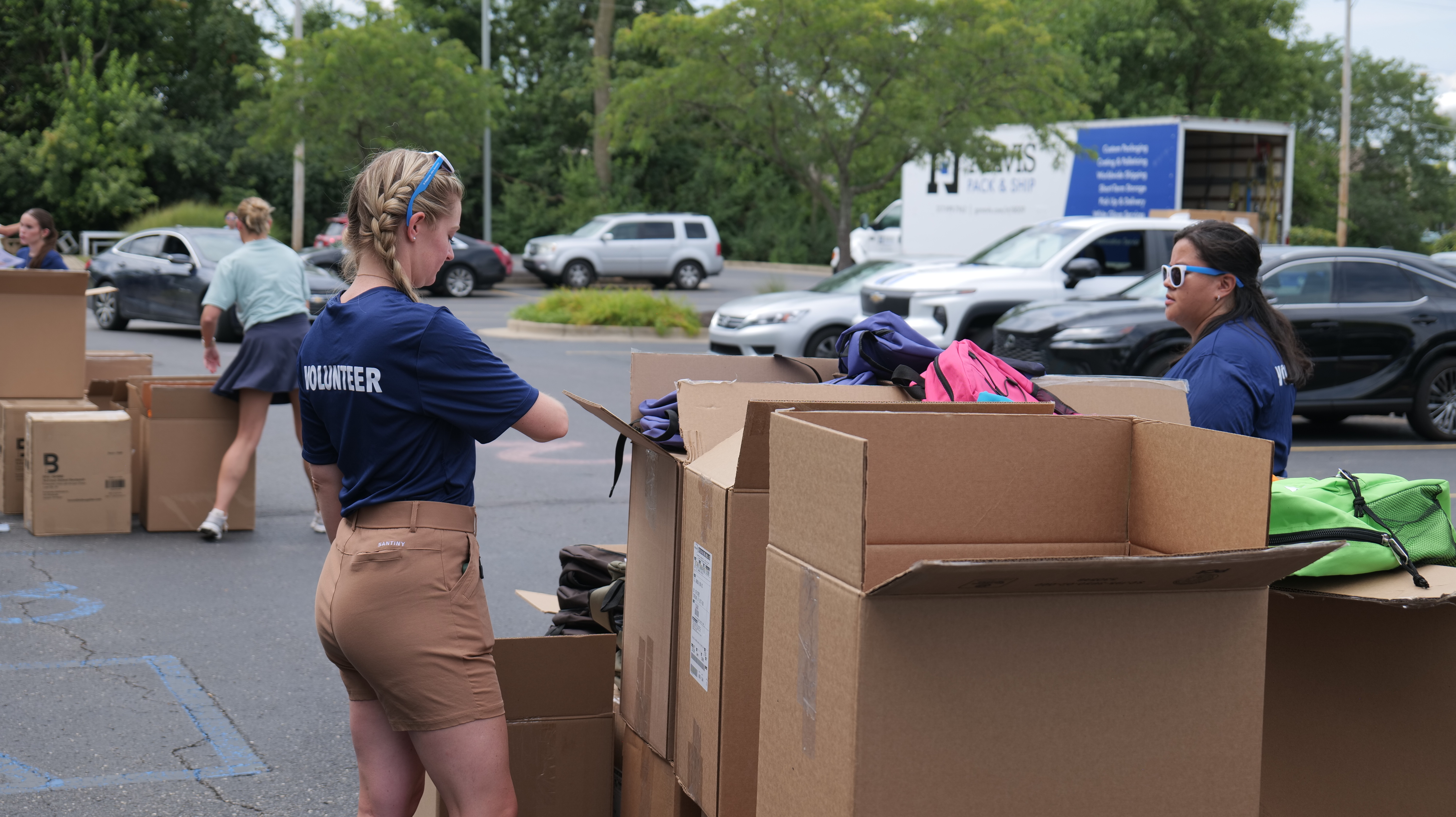 Volunteers loading boxes of donated items into a truck in a parking lot.