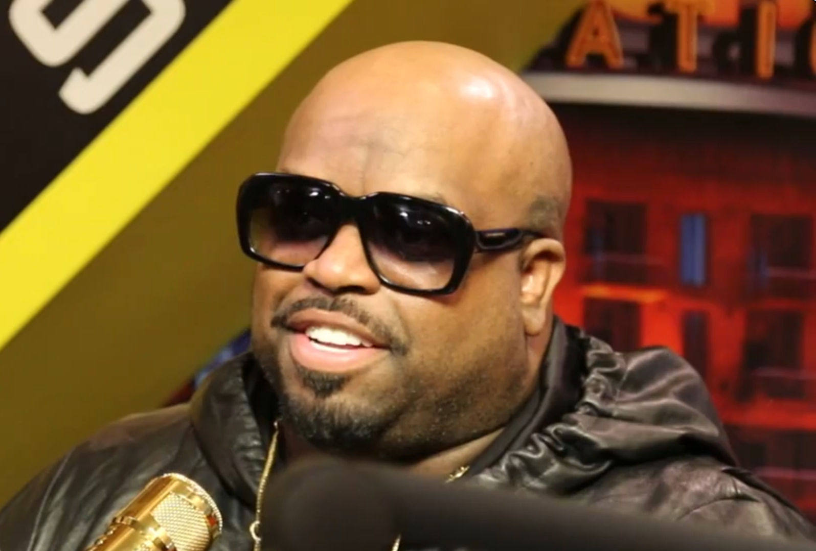 A bald man with a beard wearing sunglasses and a black jacket, smiling at the camera.